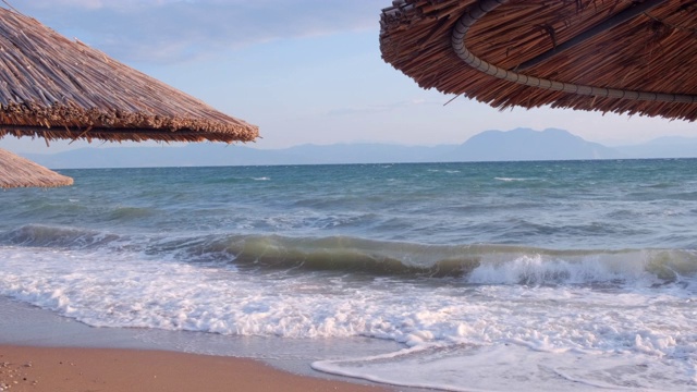 海景海洋和美丽的海景热带海滩透过茅草伞。空旷的沙滩上的背景清澈的绿松石海。节日的概念视频素材