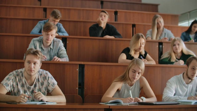 多民族学生在课堂上听讲师讲课，并在笔记本上写作。聪明的年轻人在大学学习视频素材