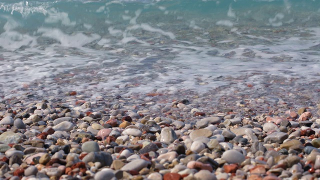 沙滩上的鹅卵石和翻滚的绿松石海浪溅起水花视频素材