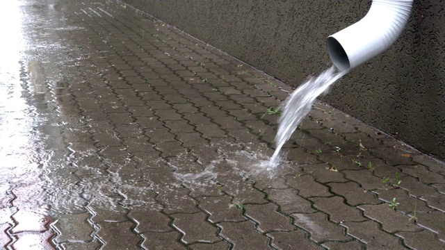 下雨时，水从一根白色排水管倾泻到人行道上。关闭了。地面视图。4 k。视频素材