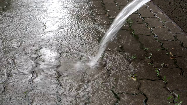 特写的水，从排水管倾泻到铺路板上，在城市的雨期间。地面视图。4 k。视频素材