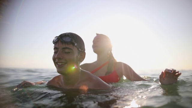 朋友们在浅海中玩耍，十几岁的女孩把男孩推入水中视频素材