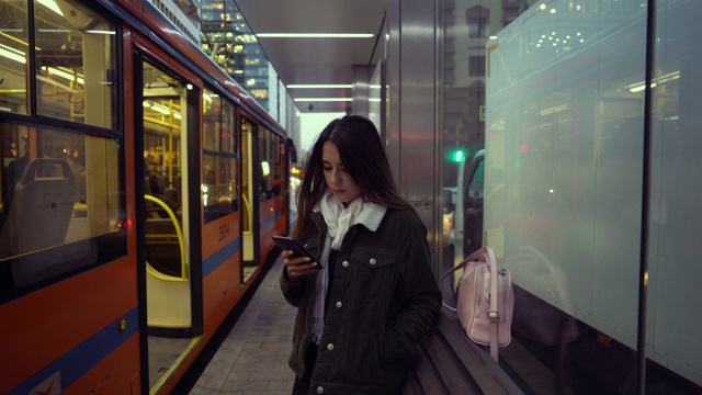 一个女孩在电车站用手机写了一条信息。视频素材