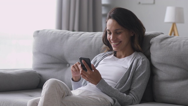 快乐的年轻女人用电话坐在家里的沙发上视频素材