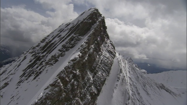 厚厚的云层在白雪覆盖的陡峭山峰的映衬下显得格外醒目。视频素材