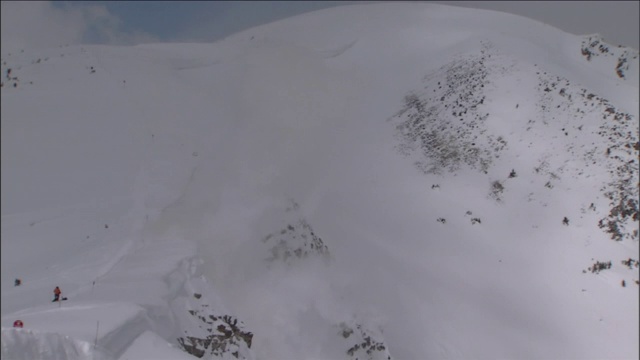 救援人员看着一场爆炸击中一个被积雪覆盖的山坡，引发雪崩。视频素材