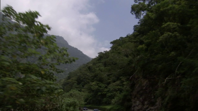 一条公路穿过郁郁葱葱的森林覆盖的山脉，乌云密布的蓝天下。视频素材