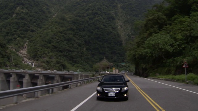 一辆轿车行驶在一条穿过郁郁葱葱、森林覆盖的山脉的道路上。视频素材