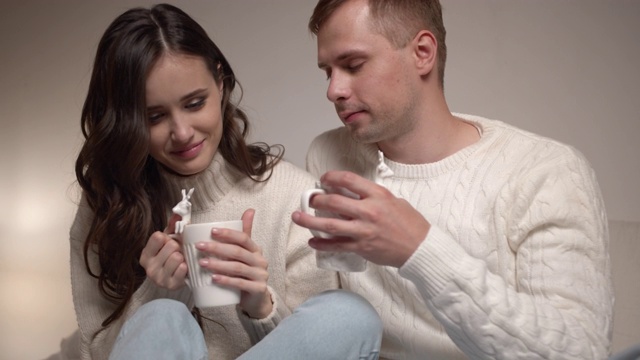 一对年轻夫妇坐在卧室的床上聊天。他们手里拿着一杯热饮，营造圣诞浪漫氛围。视频素材