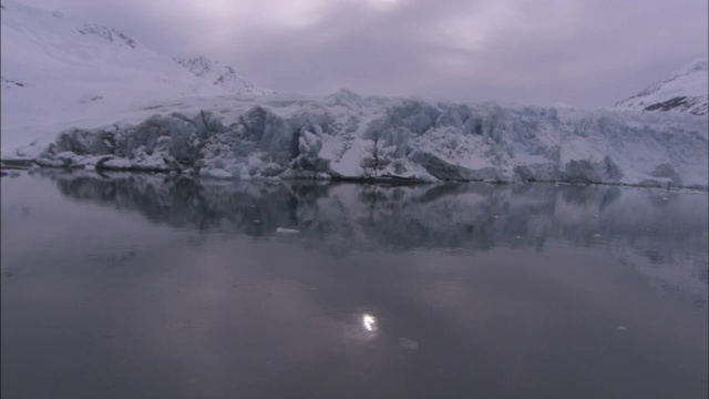 平静冰冷的海水反射出微弱的阳光和雪白的冰川。视频素材