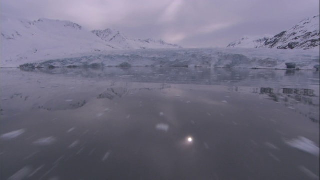 平静冰冷的海水反射出微弱的阳光和雪白的冰川。视频素材