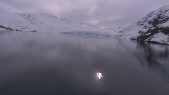 平静冰冷的海水反射出微弱的阳光和雪白的冰川。视频素材