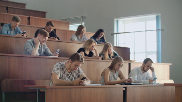 在一场无聊的大学讲座中，学生们看着智能手机的屏幕。许多人视频素材