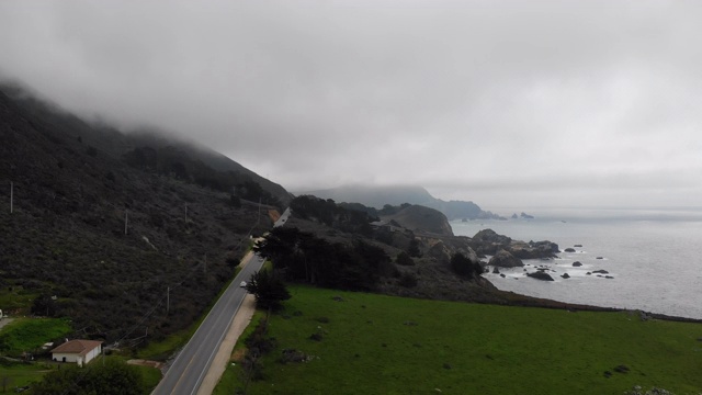 bs34_快速向后飞过一条公路，旁边是大山和草地，有悬崖俯瞰海洋。汽车慢慢驶过。乌云笼罩着山顶视频素材