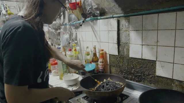 亚洲年轻女孩准备混合意大利食物烹饪黑色意大利面与鱼，拍摄膳食与移动相机。视频素材