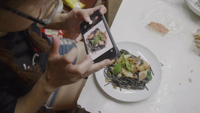 亚洲年轻女孩准备混合意大利食物烹饪黑色意大利面与鱼，拍摄膳食与移动相机。视频素材