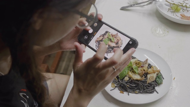 亚洲年轻女孩准备混合意大利食物烹饪黑色意大利面与鱼，拍摄膳食与移动相机。视频素材