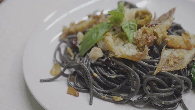 亚洲年轻女孩准备混合意大利食物烹饪黑色意大利面与鱼，拍摄膳食与移动相机。视频素材