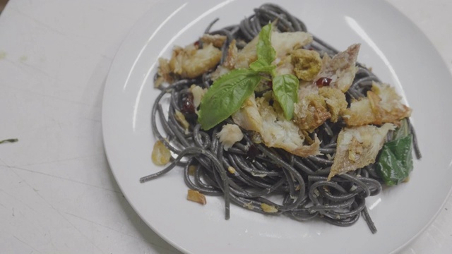 亚洲年轻女孩准备混合意大利食物烹饪黑色意大利面与鱼，拍摄膳食与移动相机。视频素材