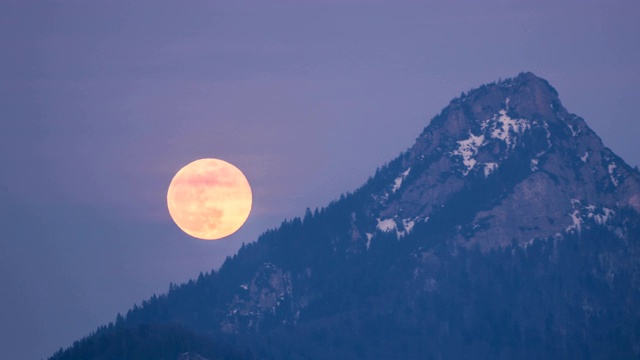 冬天的夜晚，一轮金色的满月升起在高山的顶峰视频素材