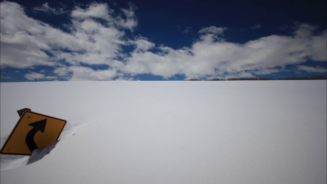 一块部分被深雪掩埋的路标上方飘着云朵。视频素材