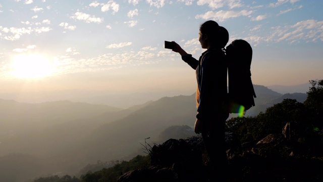 一位女性徒步旅行者用手机拍下了山上日落的照片视频素材