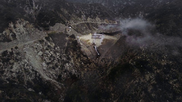 从空中拍摄的水从一个大坝附近的蜿蜒道路在树木繁茂的山区视频素材