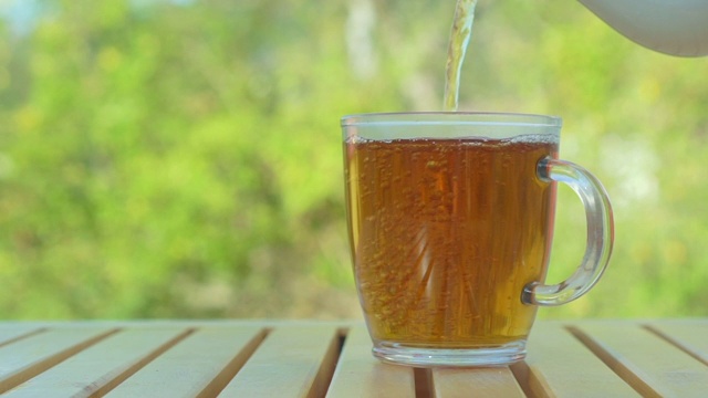 以绿色自然为背景，将茶从茶壶倒入杯中视频素材