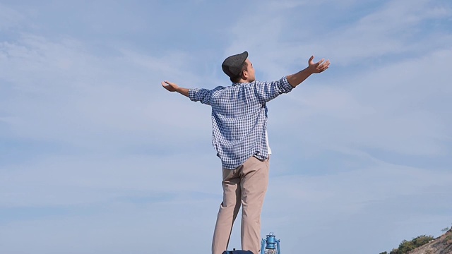 亚洲男人举起双手，与蓝天和顶山景，生活理念。缓慢的运动。视频素材