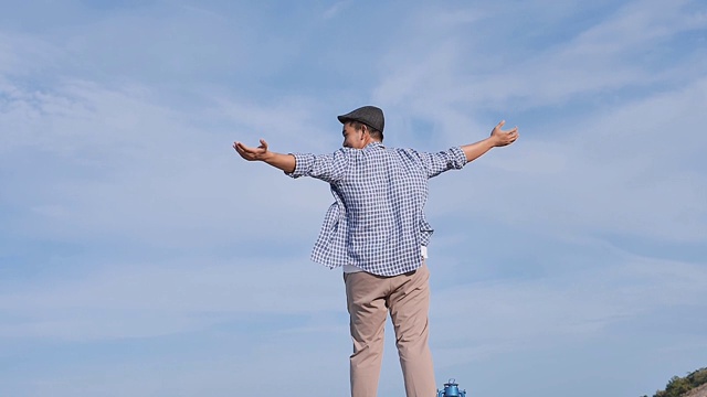 亚洲男人举起双手，与蓝天和顶山景，生活理念。缓慢的运动。视频素材