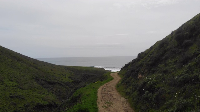 沿着绿色山上的小路，远处海浪汹涌。视频下载