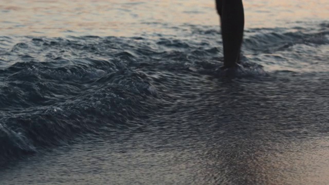 一个女人走在海滩上，用她的腿泼水视频素材