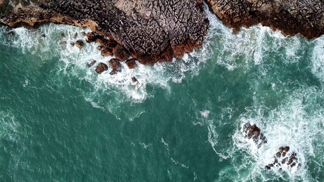 无人机空中俯瞰海浪撞击海滩上的岩石与绿松石海水视频素材