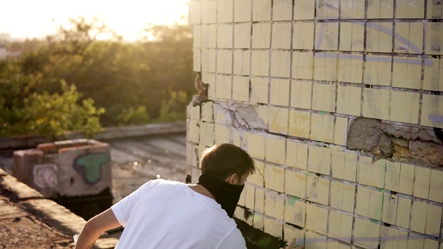 城市街头艺术家是站在街道建筑墙壁附近，用喷雾剂喷漆。现代艺术与青年创意观念。戴着黑色面具。在户外视频素材