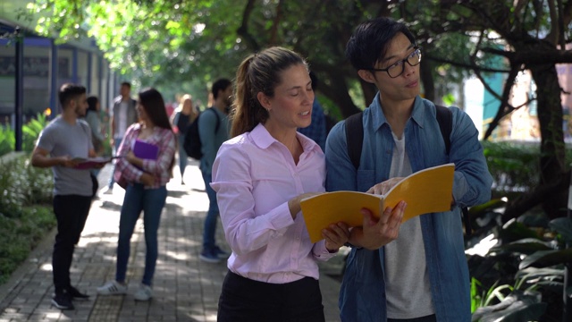 女老师在大学校园里帮助一个交换学生，一边看笔记本一边解释一些事情视频素材