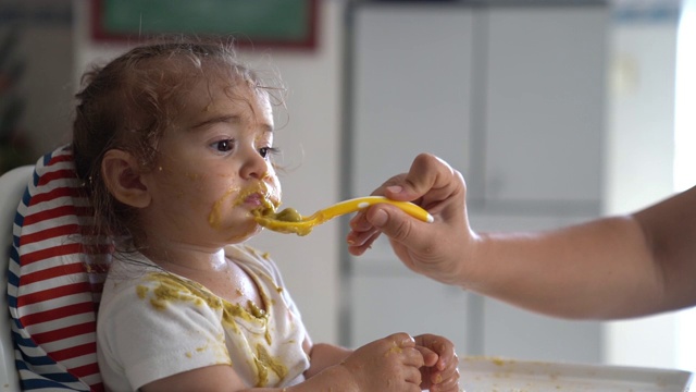 慢动作高清视频的婴儿女孩坐在喂食椅和吃婴儿食品视频素材