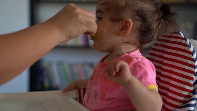 慢动作高清视频的婴儿女孩坐在喂食椅和吃婴儿食品视频素材