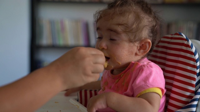 慢动作高清视频的婴儿女孩坐在喂食椅和吃婴儿食品视频素材