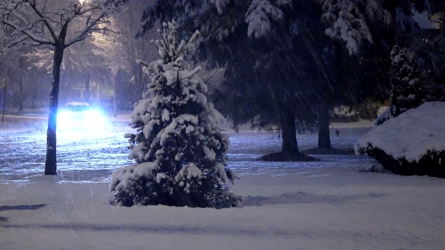 汽车行驶缓慢，在积雪覆盖的居民区街道上，夜间车灯自然在冬夜穿行视频素材