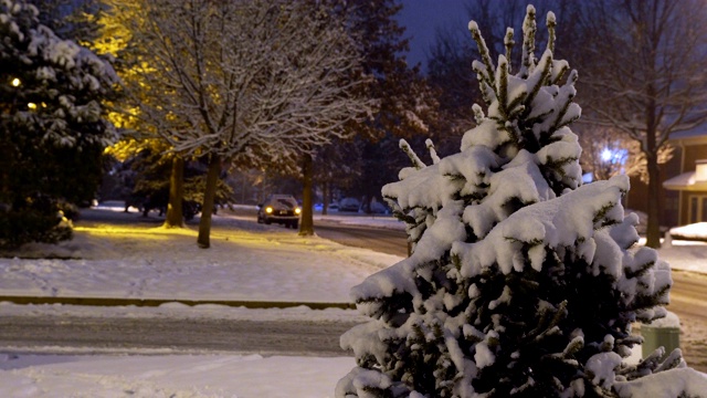 车灯在夜里在小区的冰路上亮着，雪花落在房子上，夜晚是冬天的时候视频素材