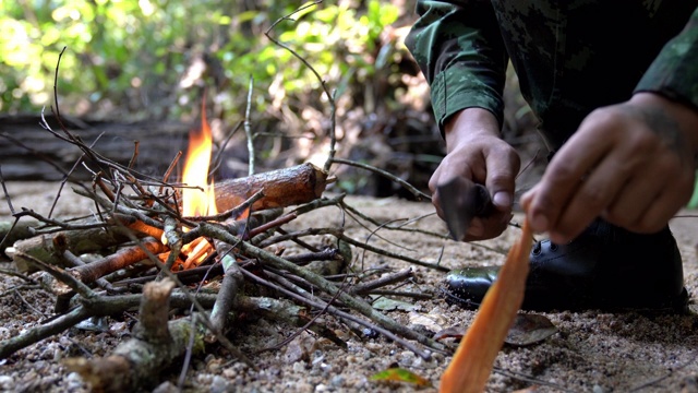 身着迷彩服的士兵用露营刀在露营区生火做饭的4K中拍摄。燃烧的火焰在雨林露营营火。视频素材