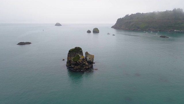 在这雾蒙蒙平静的日子里，海湾里的岩石和停泊着的游艇。加利福尼亚西海岸特立尼达附近的太平洋。空中视频与电影轨道摄像机运动。视频素材