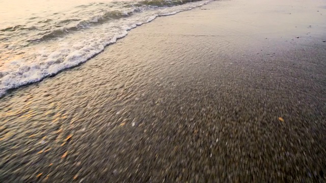 海岸边的沙带着平静的波涛溅起沙滩，波夫掠过水面视频素材