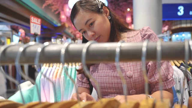 年轻的亚洲女人在购物中心的服装店购物的场景慢镜头，假期周末的概念，亚洲女人的生活方式视频素材