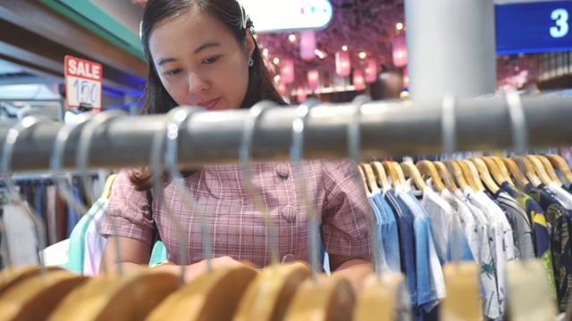 年轻的亚洲女人在购物中心的服装店购物的场景慢镜头，假期周末的概念，亚洲女人的生活方式视频素材