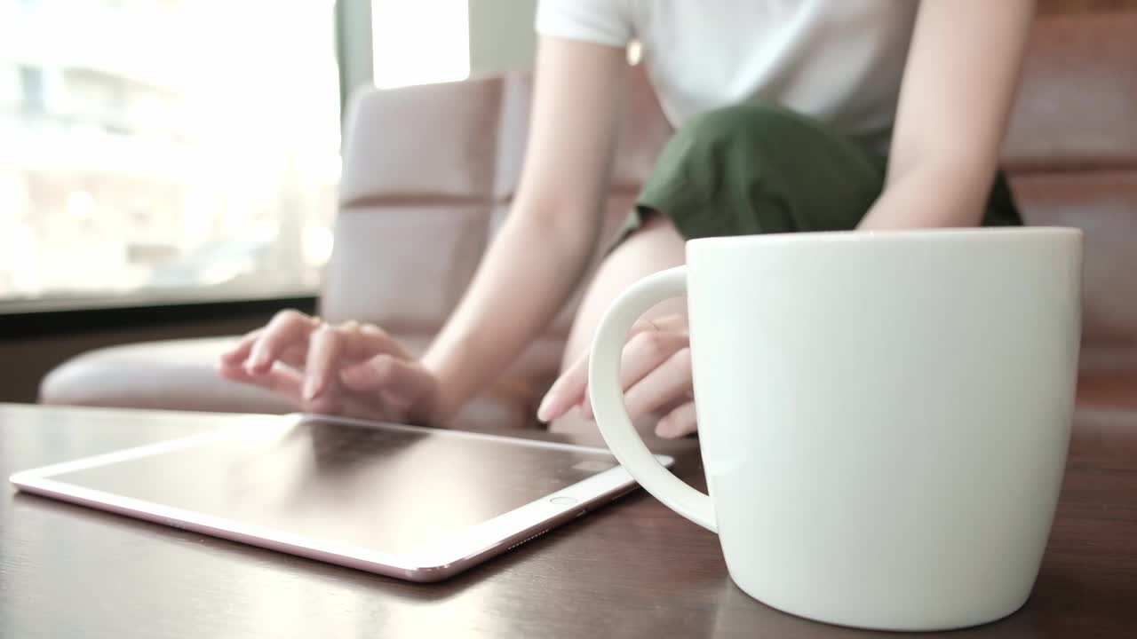 一名亚洲女性在咖啡店里一边喝咖啡一边用平板电脑聊天。视频素材