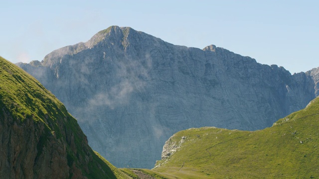 难以辨认的徒步旅行者走在陡峭的山地草地上视频素材