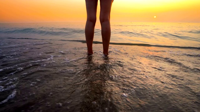 女人的脚溅在海滩上的海浪日落。在美丽的海滩上，海水溅在脚上，这是一幅宁静放松的画面视频素材