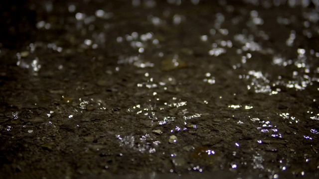 雨水溅落在被水淹没的沥青路面上。Loopable背景视频素材