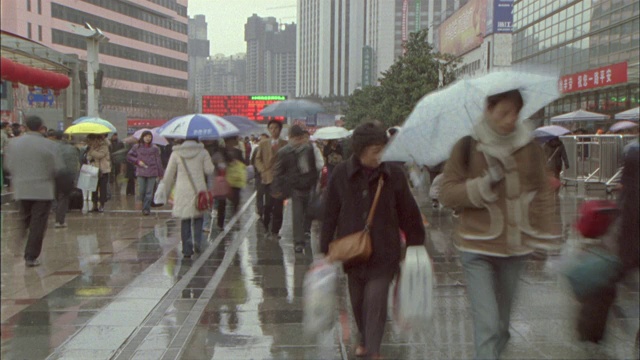 行人撑着雨伞匆匆走过下着雨的街道。视频素材